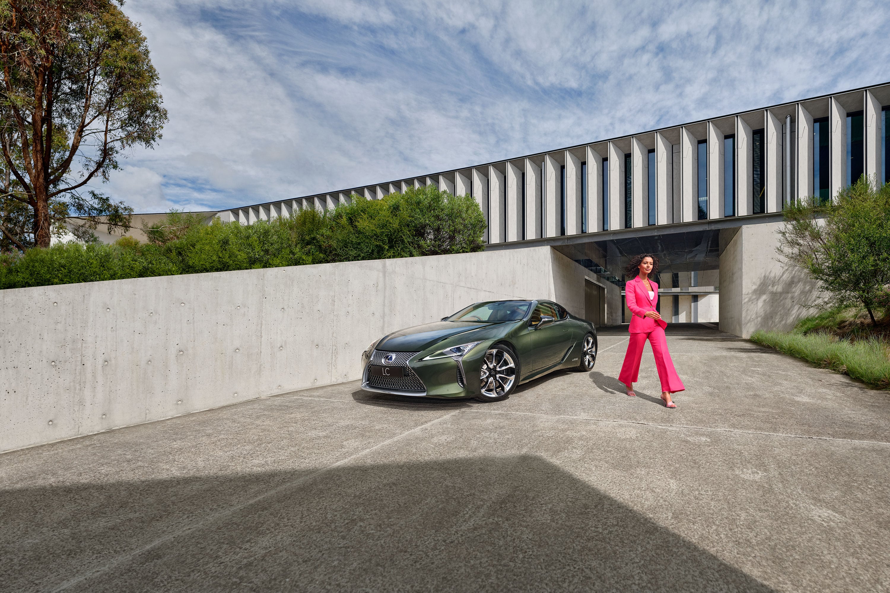 Woman dressed in a bright pink suit walks away from a Lexus LC coupe in Khaki Metal